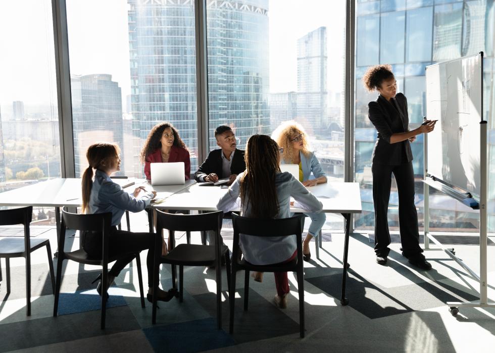 African American female presents on a whiteboard to a meeting