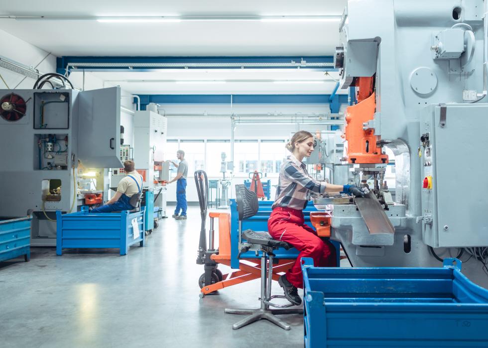 Wide view of factory workers producing metal parts on punching machine
