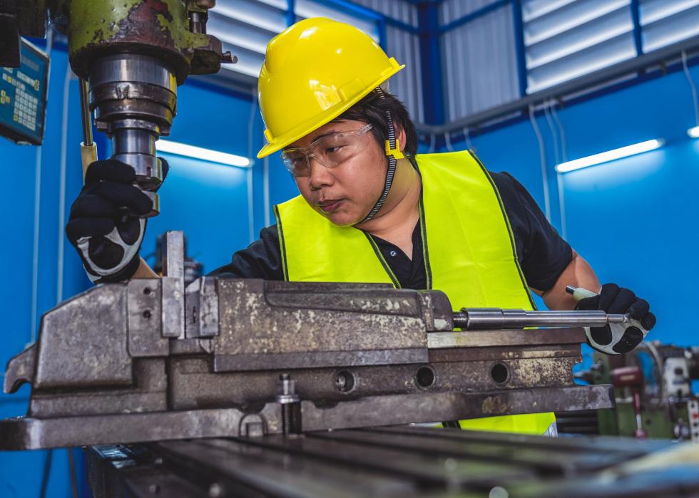 Machinist in safety suit operating a lathe in metalworking factory
