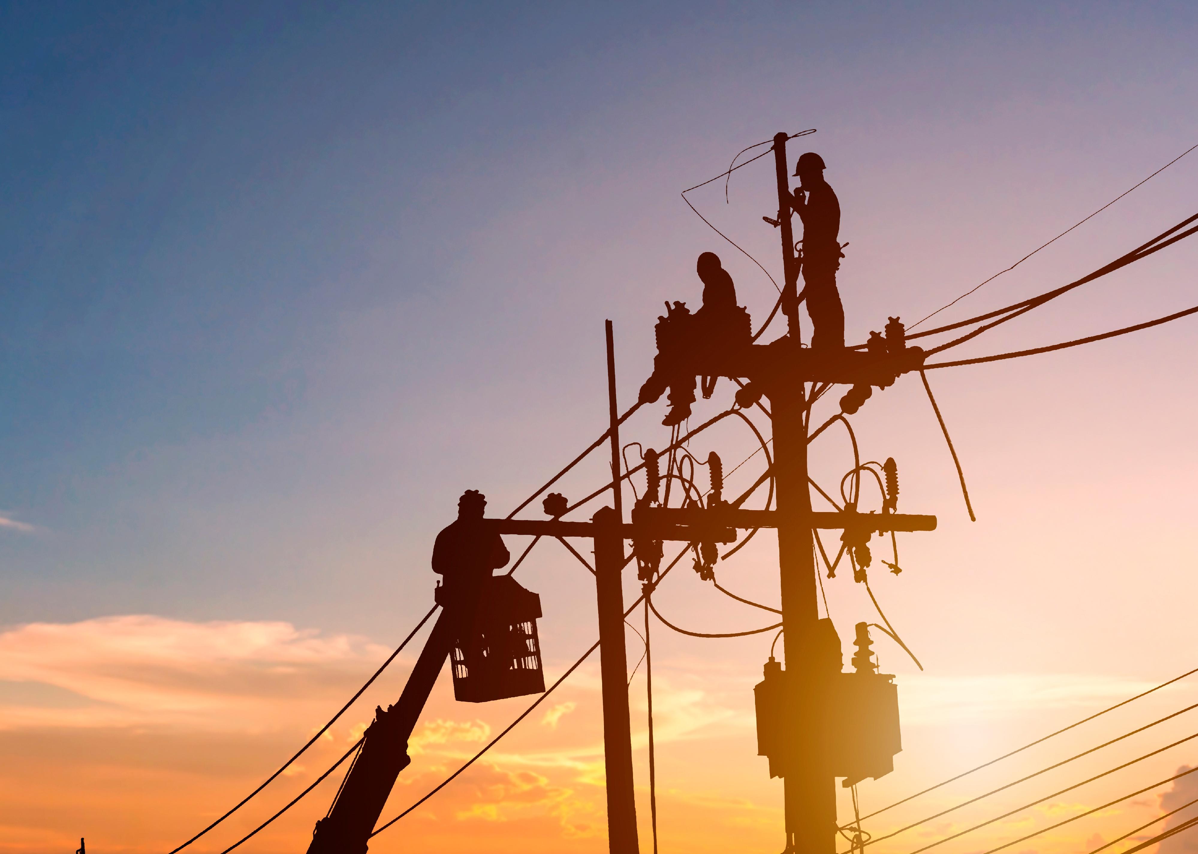 Silhouetted electrician working on poles to install high-voltage equipment.