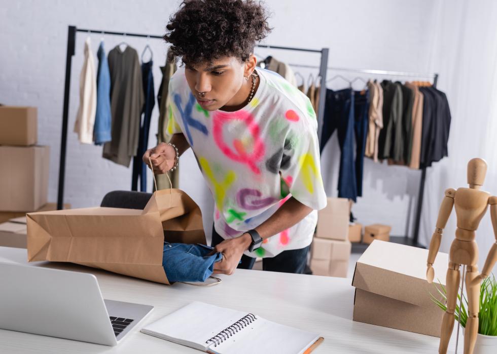 A young person looking at a computer order and filling a shopping bag. 