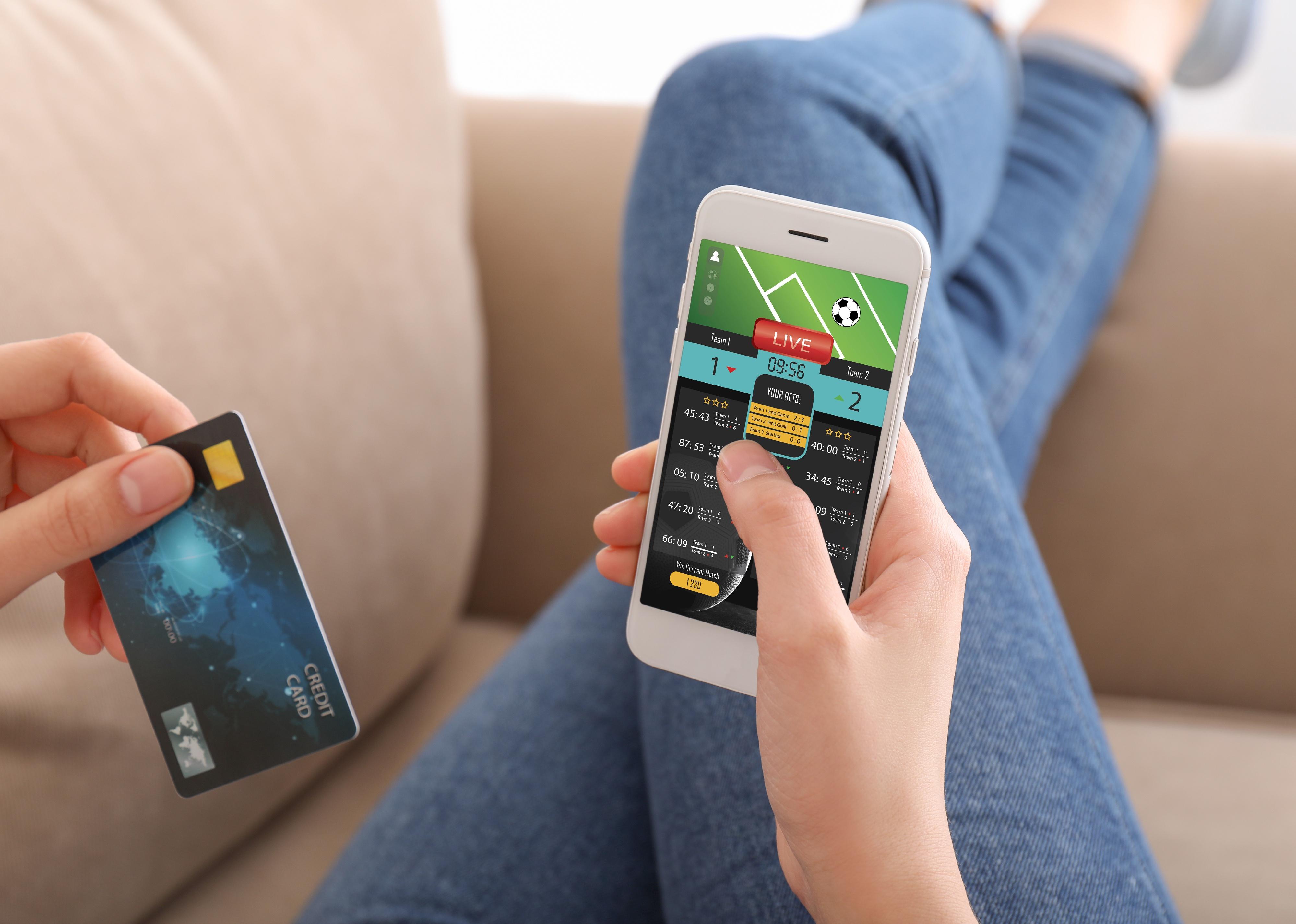 Young adult with credit card placing sports bet at home.