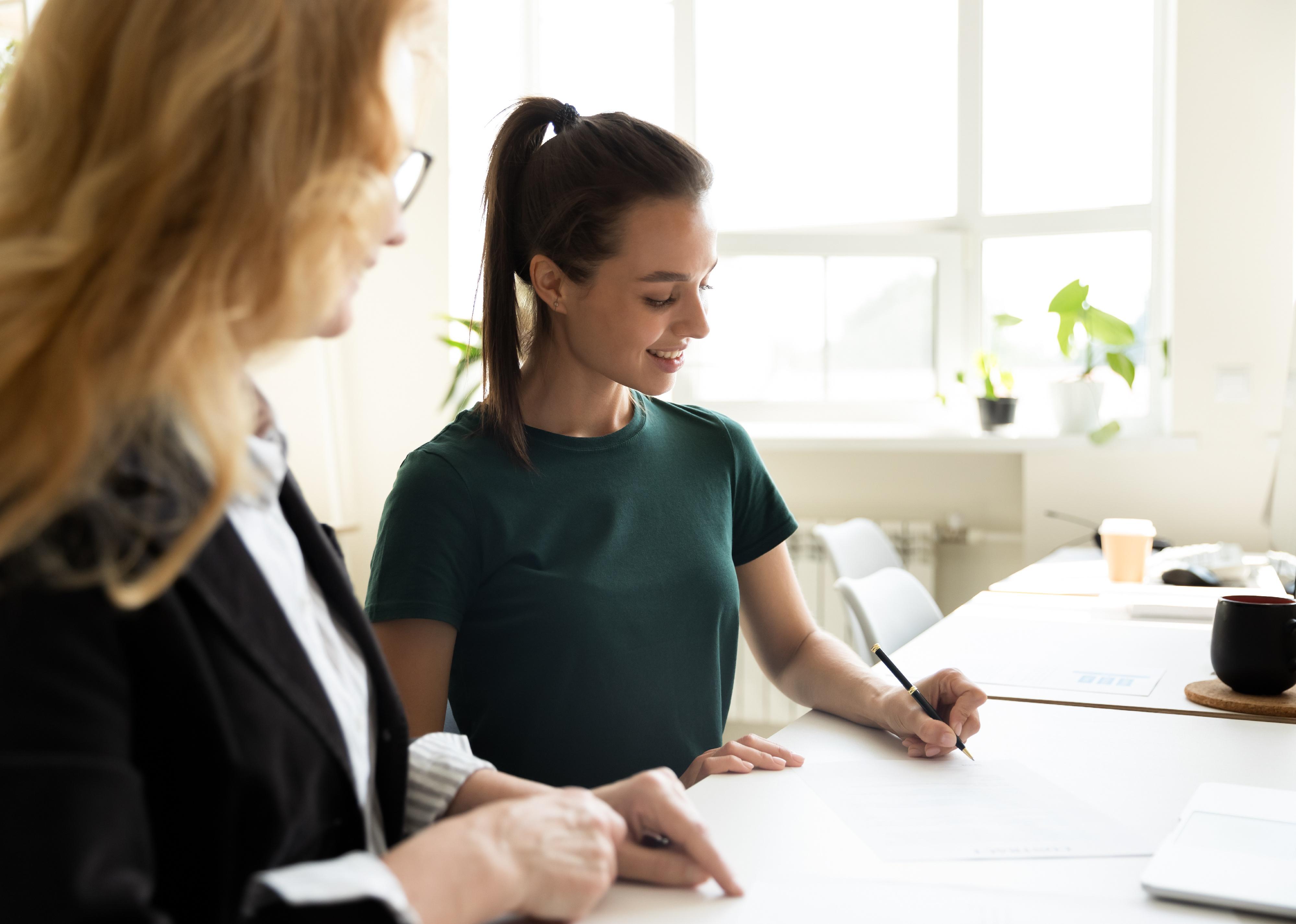 Two women at a table with one signing papers