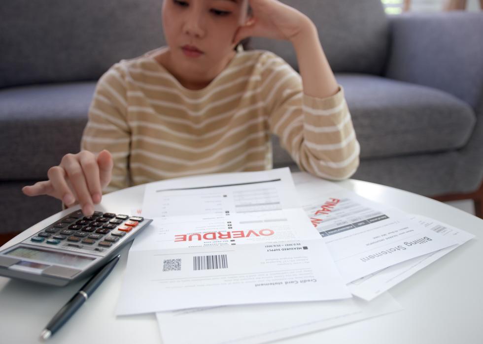 Asian woman using calculator next to overdue notices