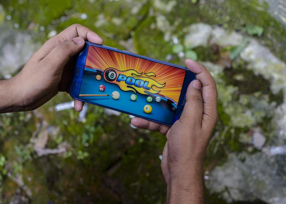 A guy playing 8 ball pool on his phone.