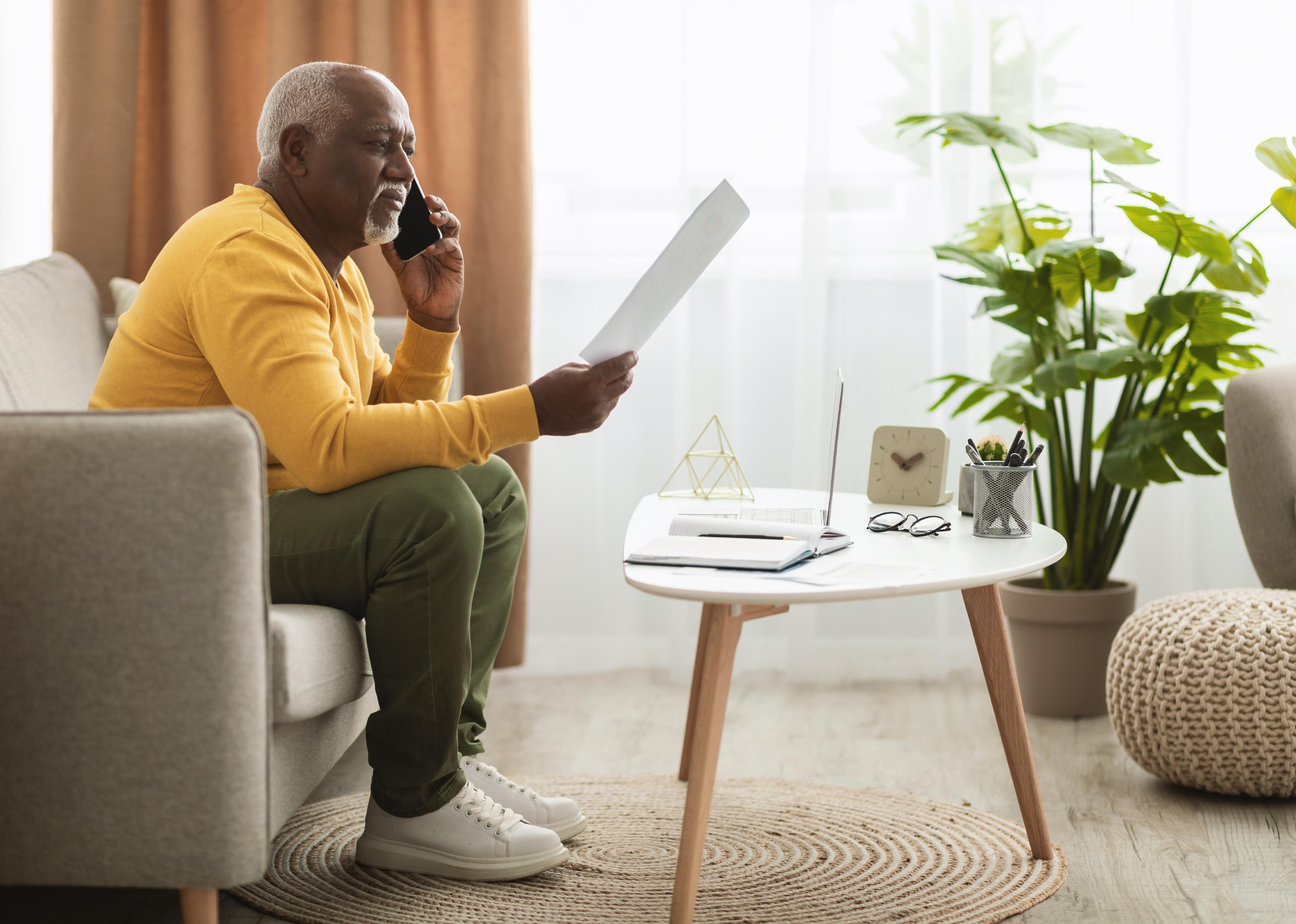 Senior talking on phone while holding paper looking concerned. 