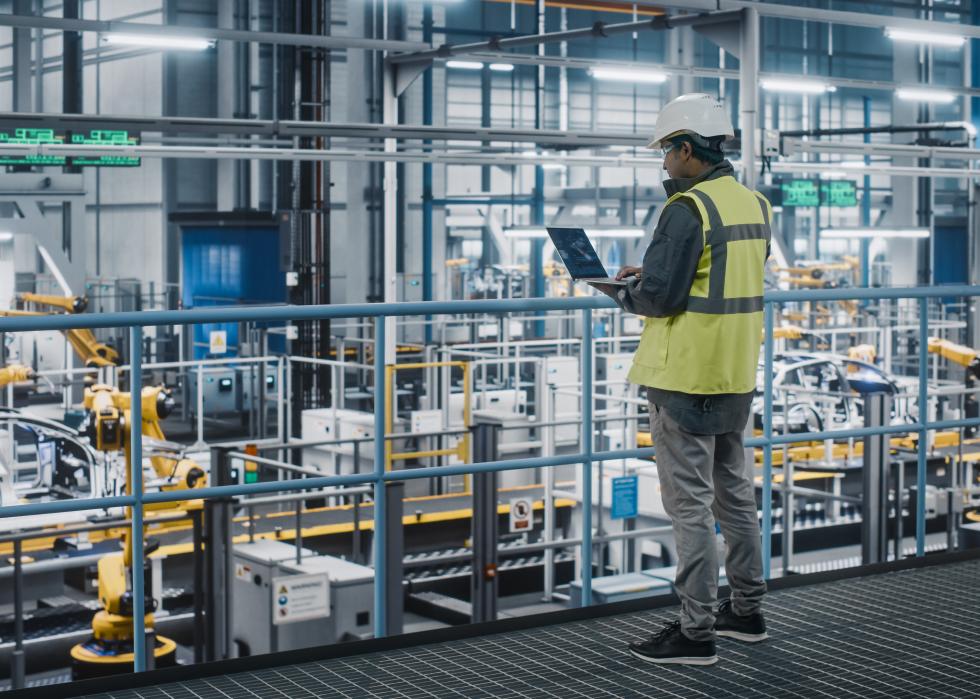 Car factory engineer in vest using laptop.