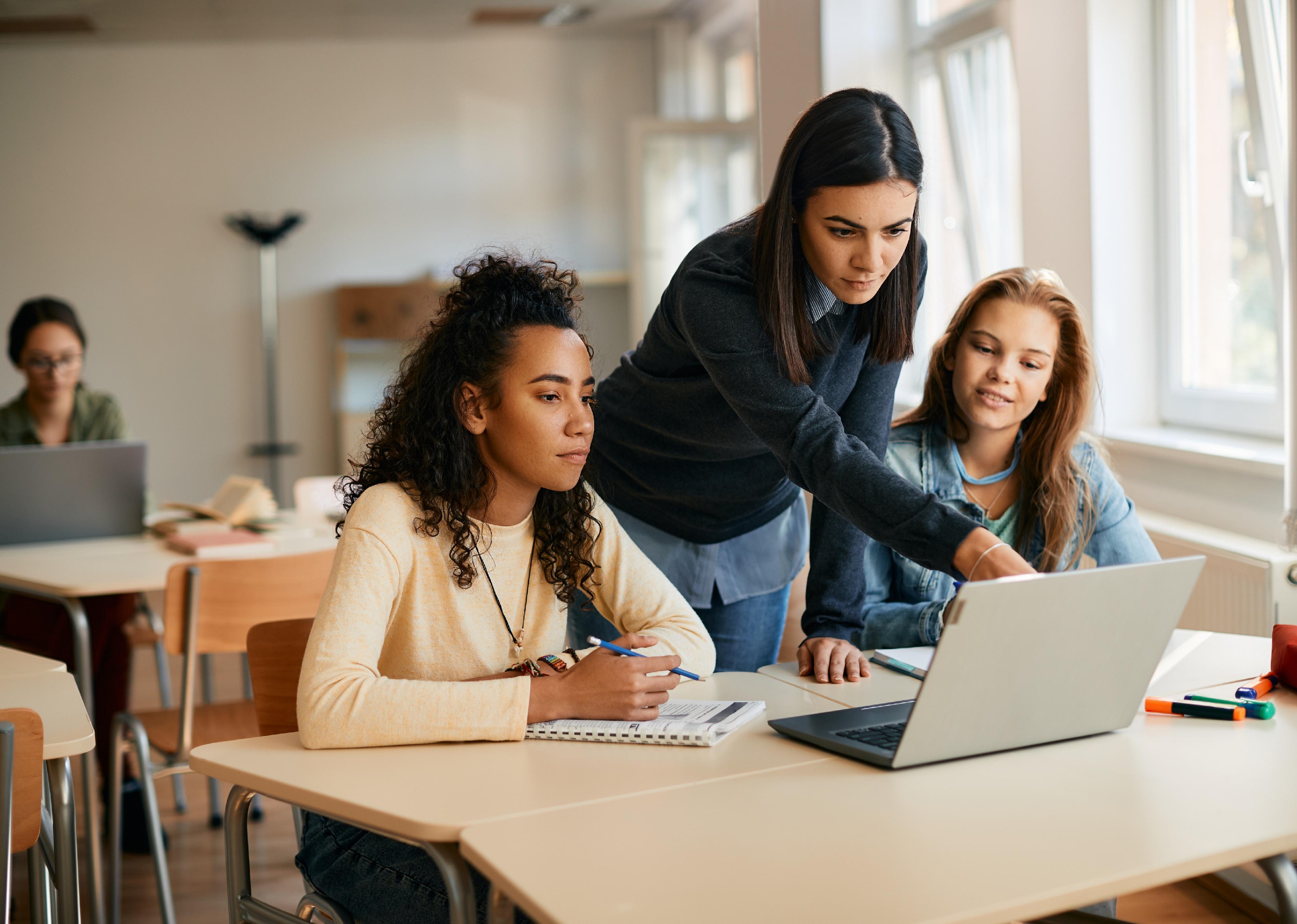 Teacher and her students using laptop during computer class in high school
