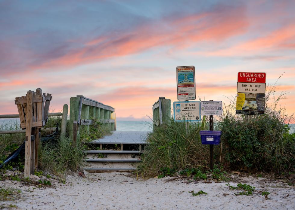 Beach access bridge and signs under sunset.