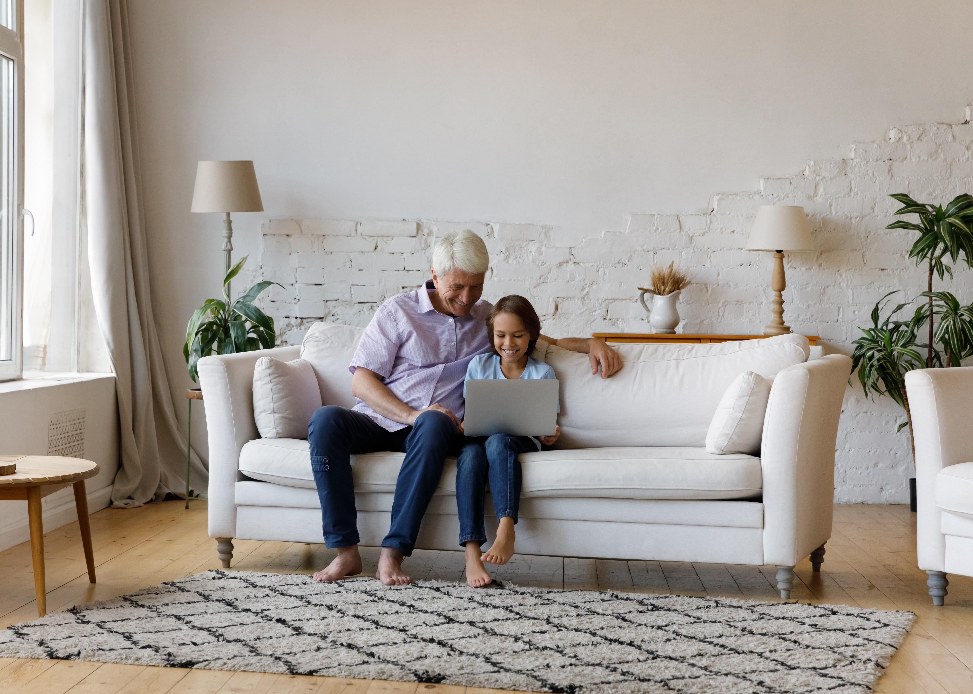 Grandpa and grandkid it on a sofa and use laptop.