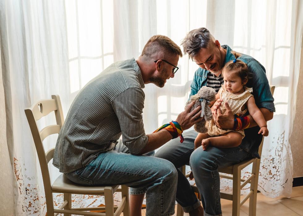 Two men sitting on chairs, playing with a little girl