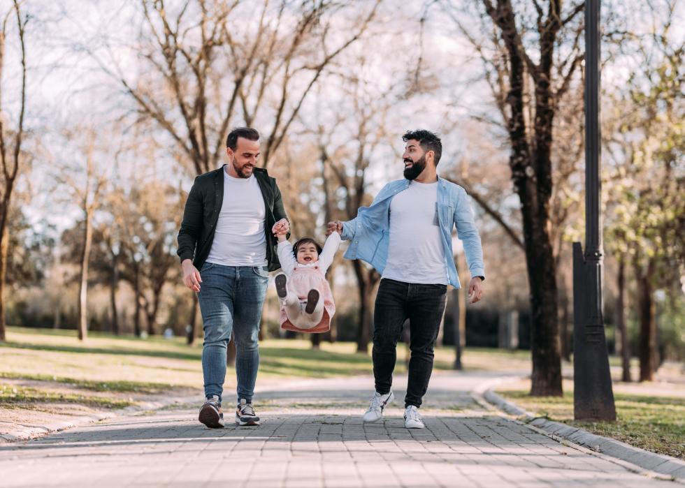Two men laughing and swinging little girl between them