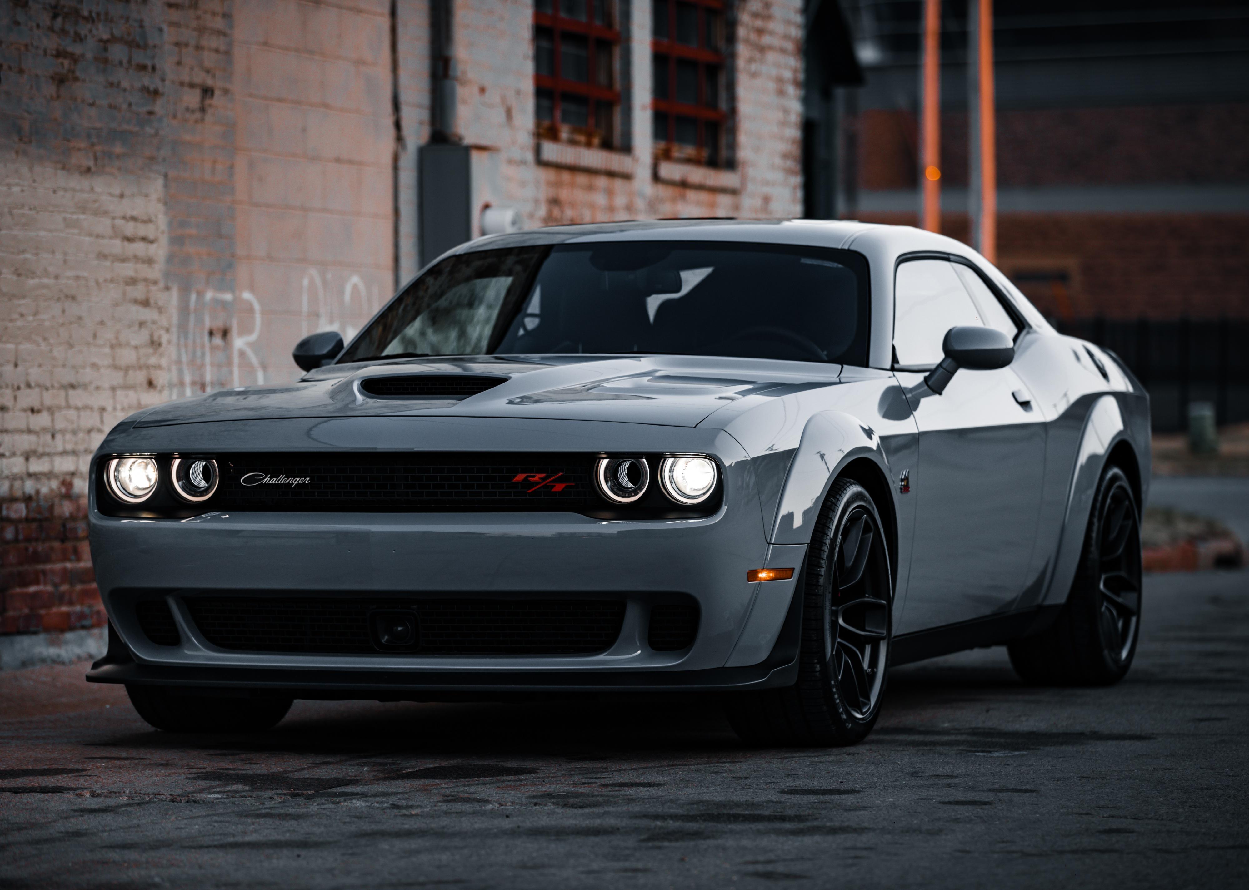 A green-gray Dodge Challenger outside by brick building.
