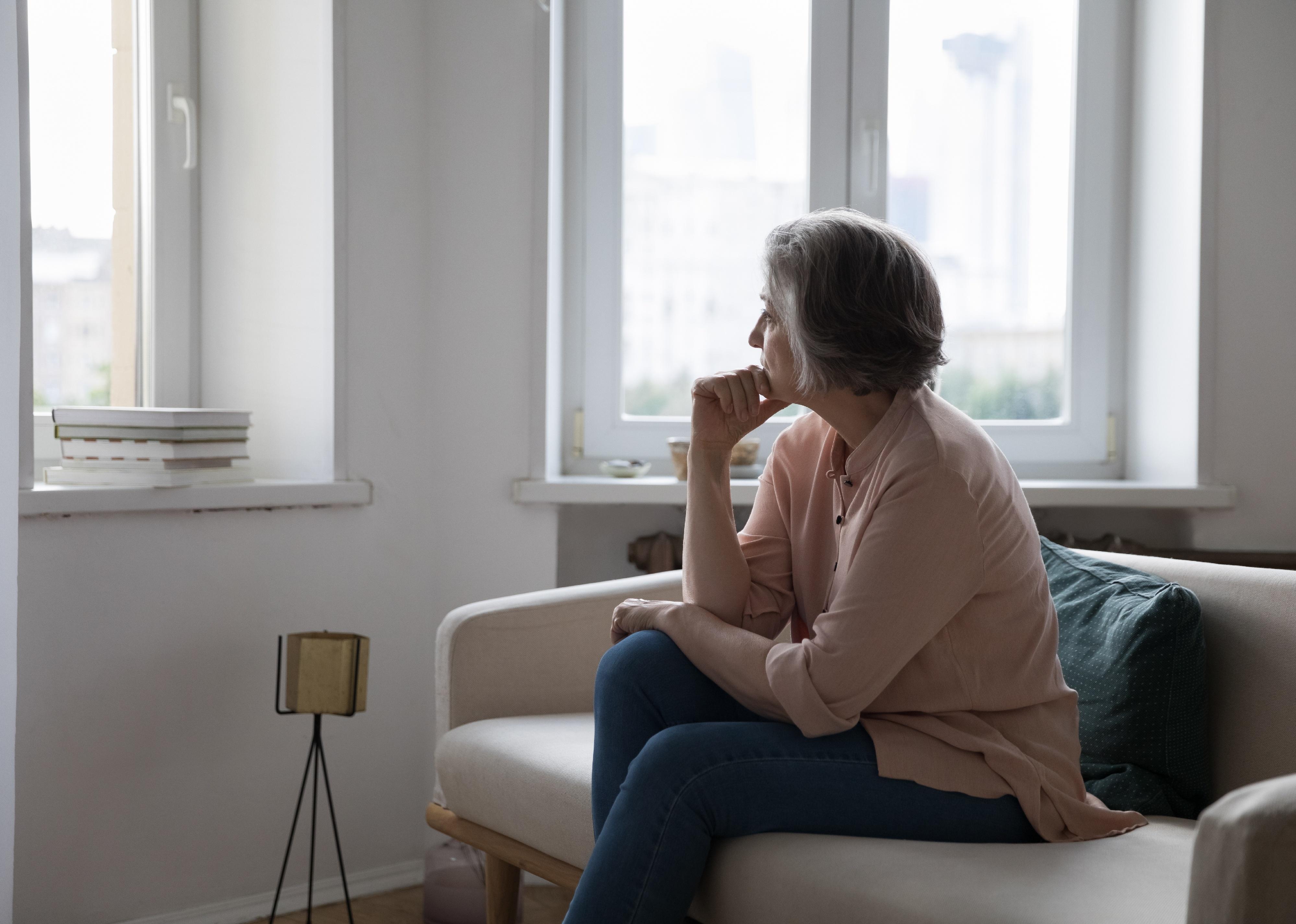 Mature lady looking out window, looking sad.