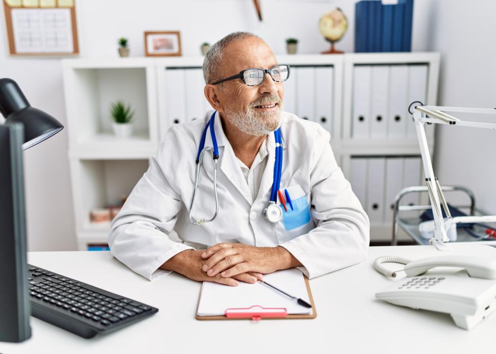 Mature doctor in an office to side with smile on face.