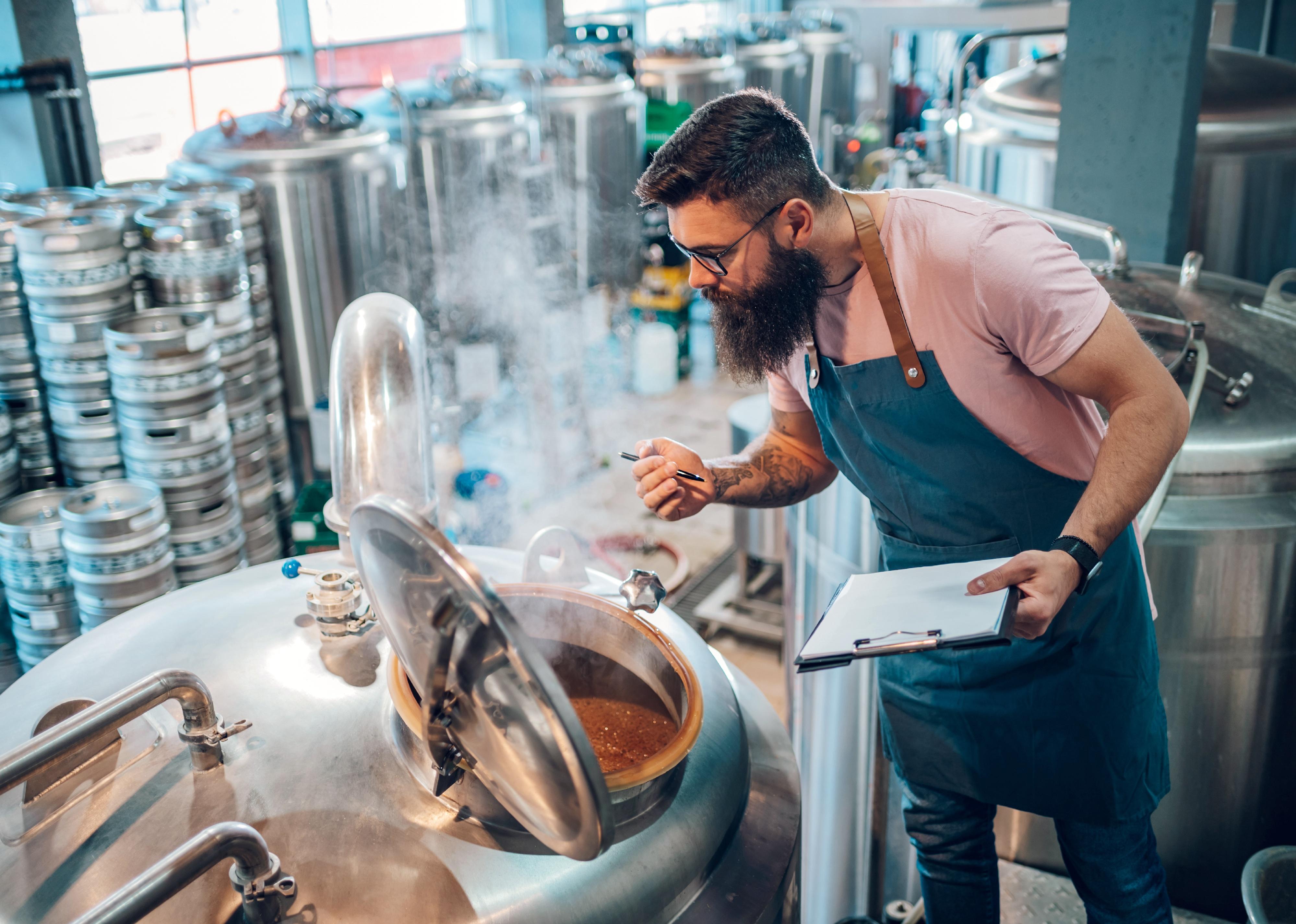 Man worker wearing an apron in a brewery using brewing equipment