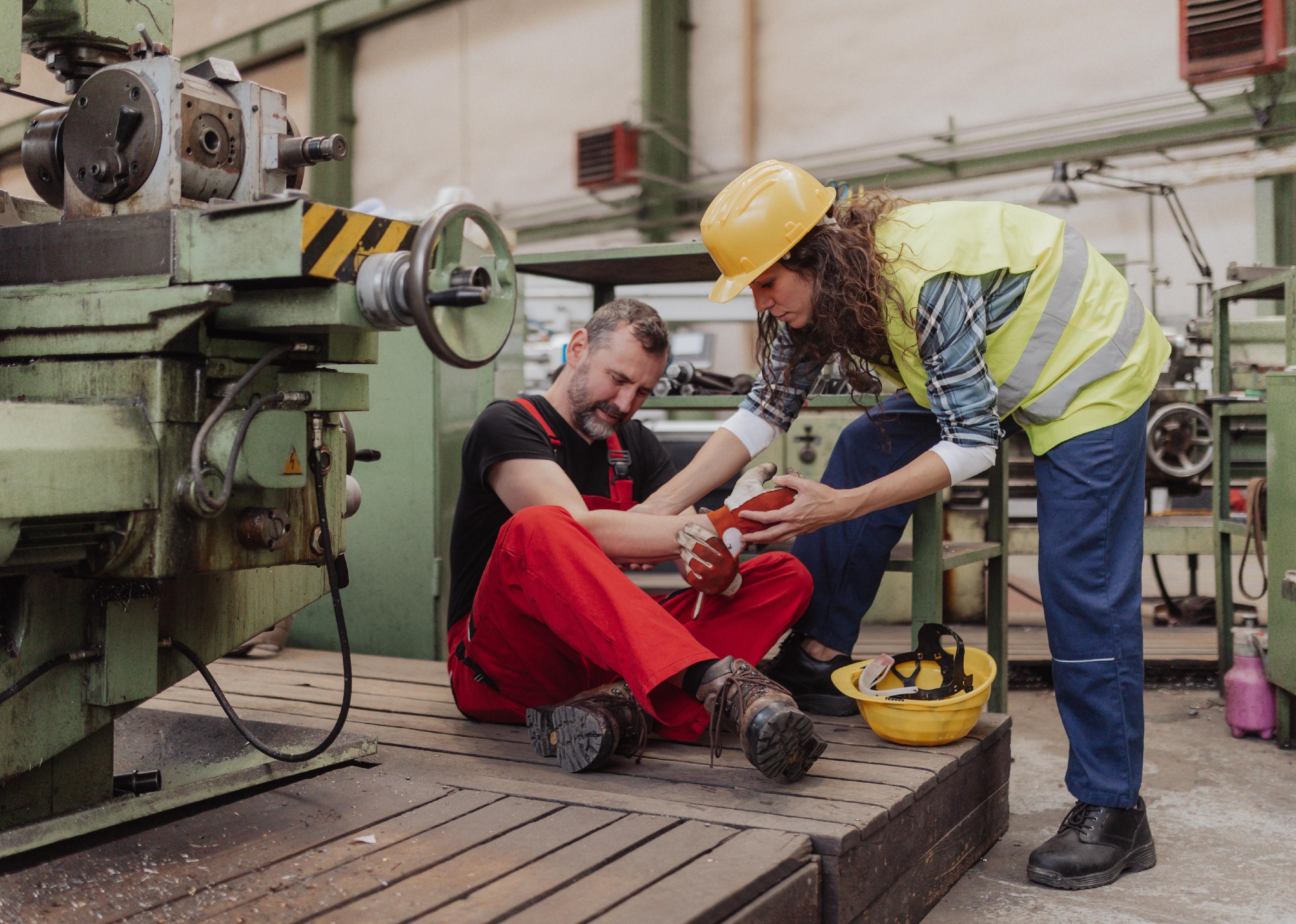 Woman is helping her colleague after accident in factory.