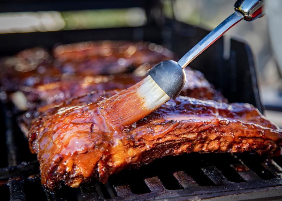 Beef ribs being basted with bbq sauce on a grill.