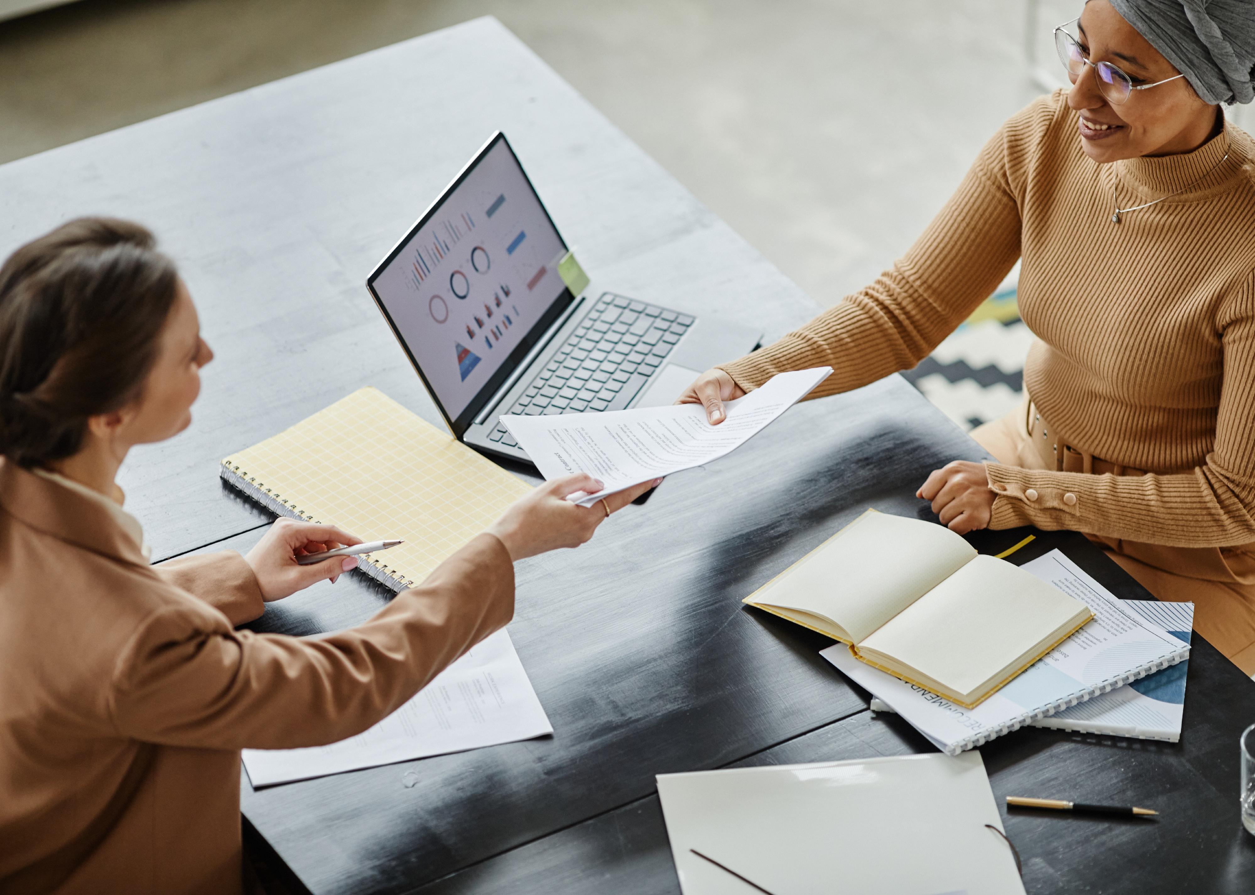 High angle of female manager handing contract to young woman in job interview