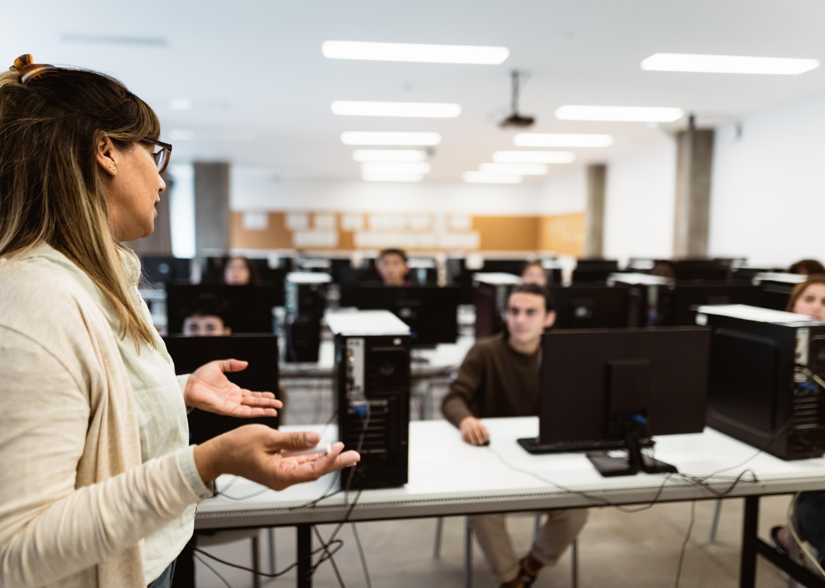Teacher lecturing at students behind computers