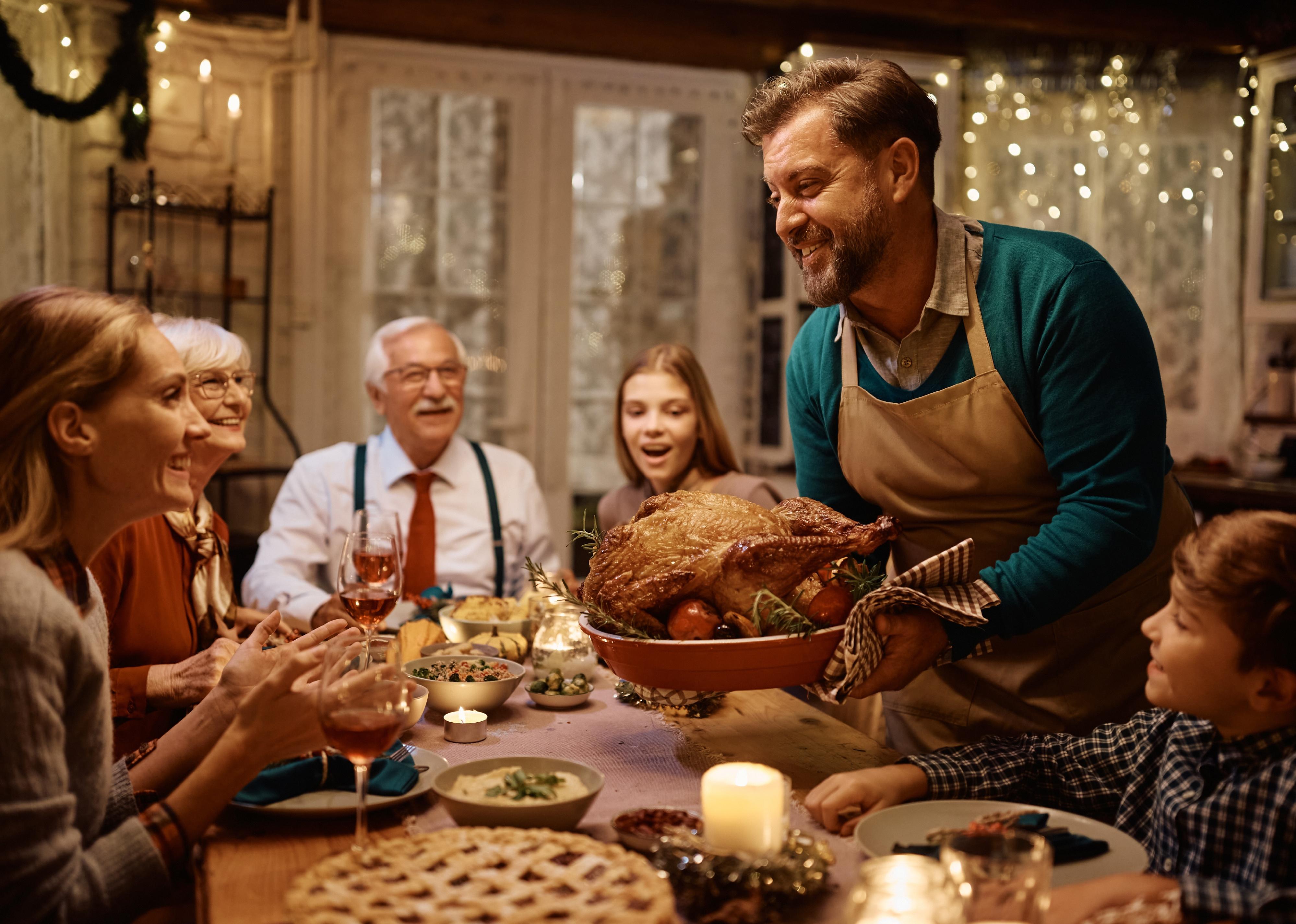 Happy man bringing roast turkey at the table during dinner.