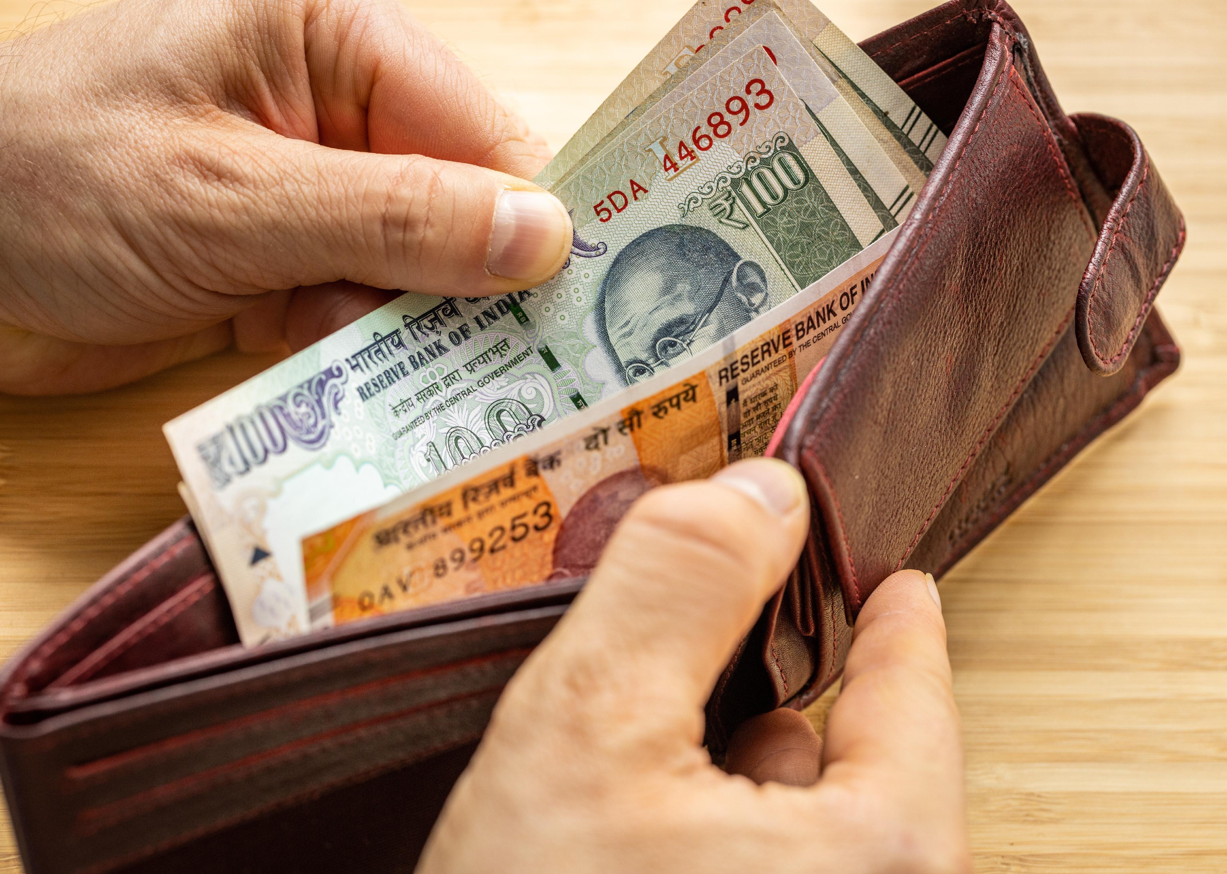 Hand takes out India Banknotes from wallet.