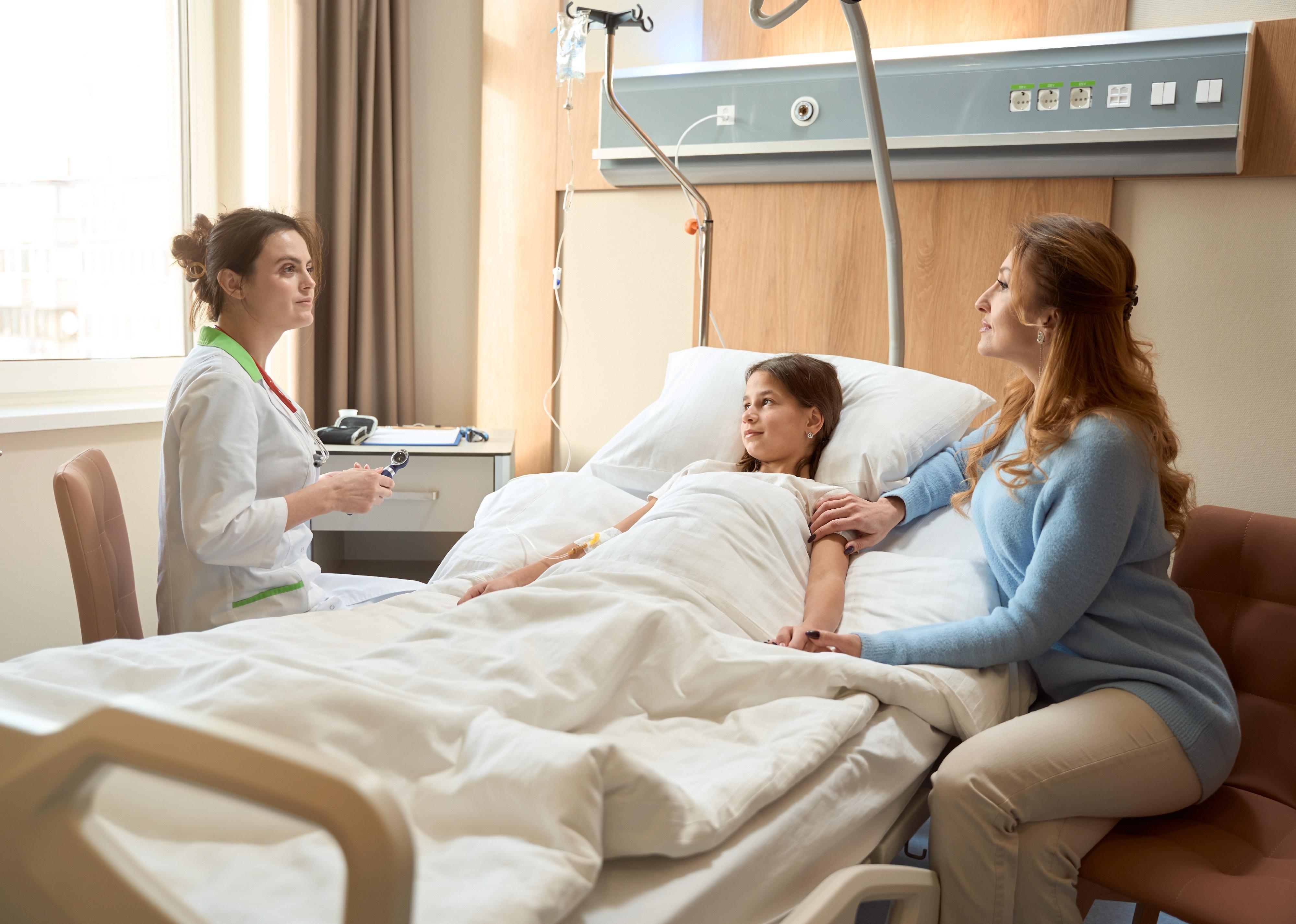 Mom and doctor communicate at the bedside of a young girl.
