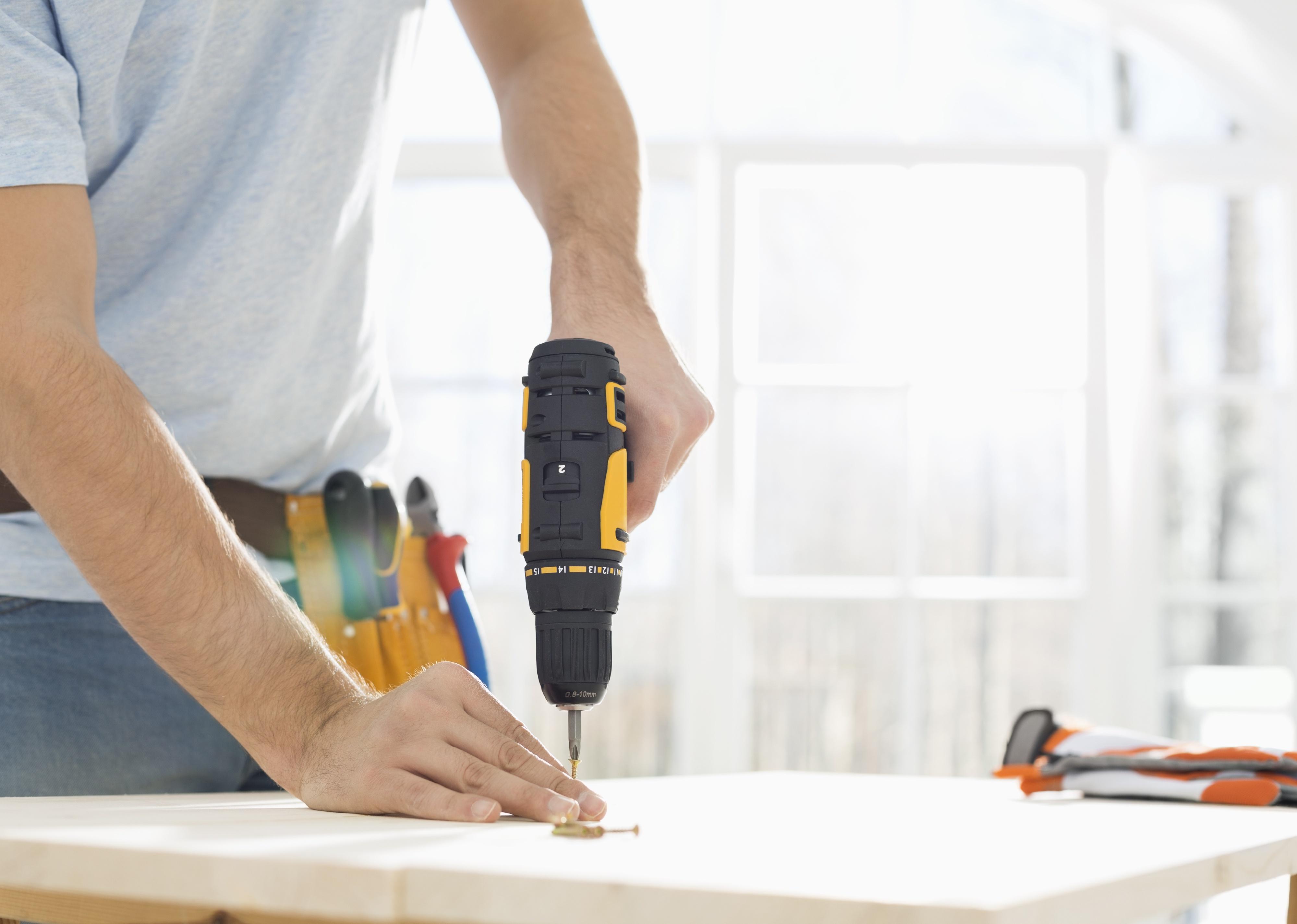 Midsection of person drilling nail on table.