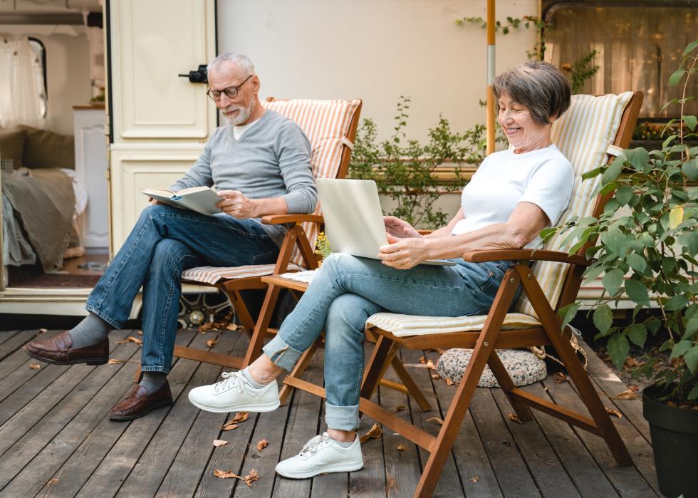 Happy senior couple reading and looking at a laptop while sitting on a porch.