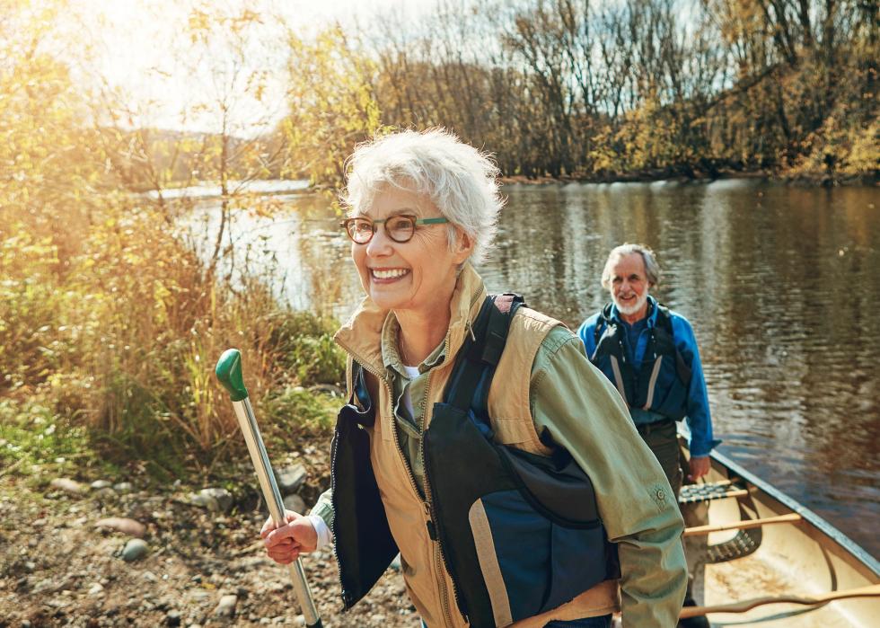 Senior woman and man smiling as they disembark from a canoe on a river.