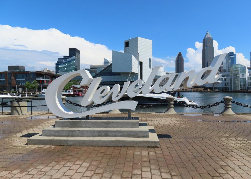 Large script sign for Cleveland with skyscraper buildings in the background.