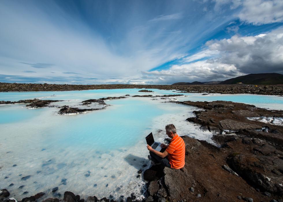 Man sitting on rock working on computer in Reykjavik, Iceland