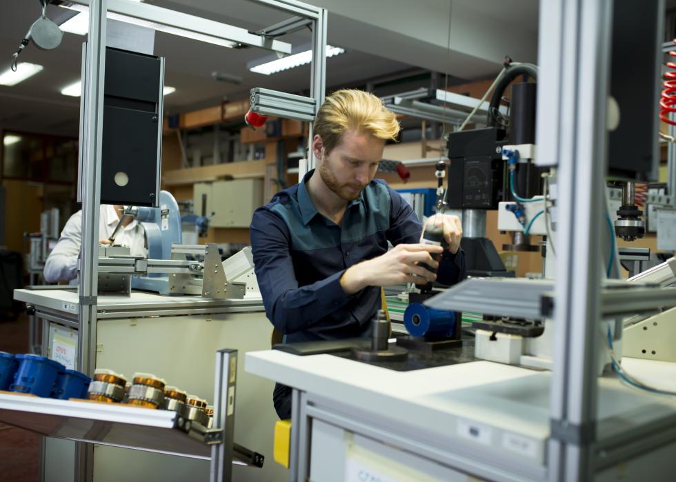 Man seated at a factory station working on a machine 