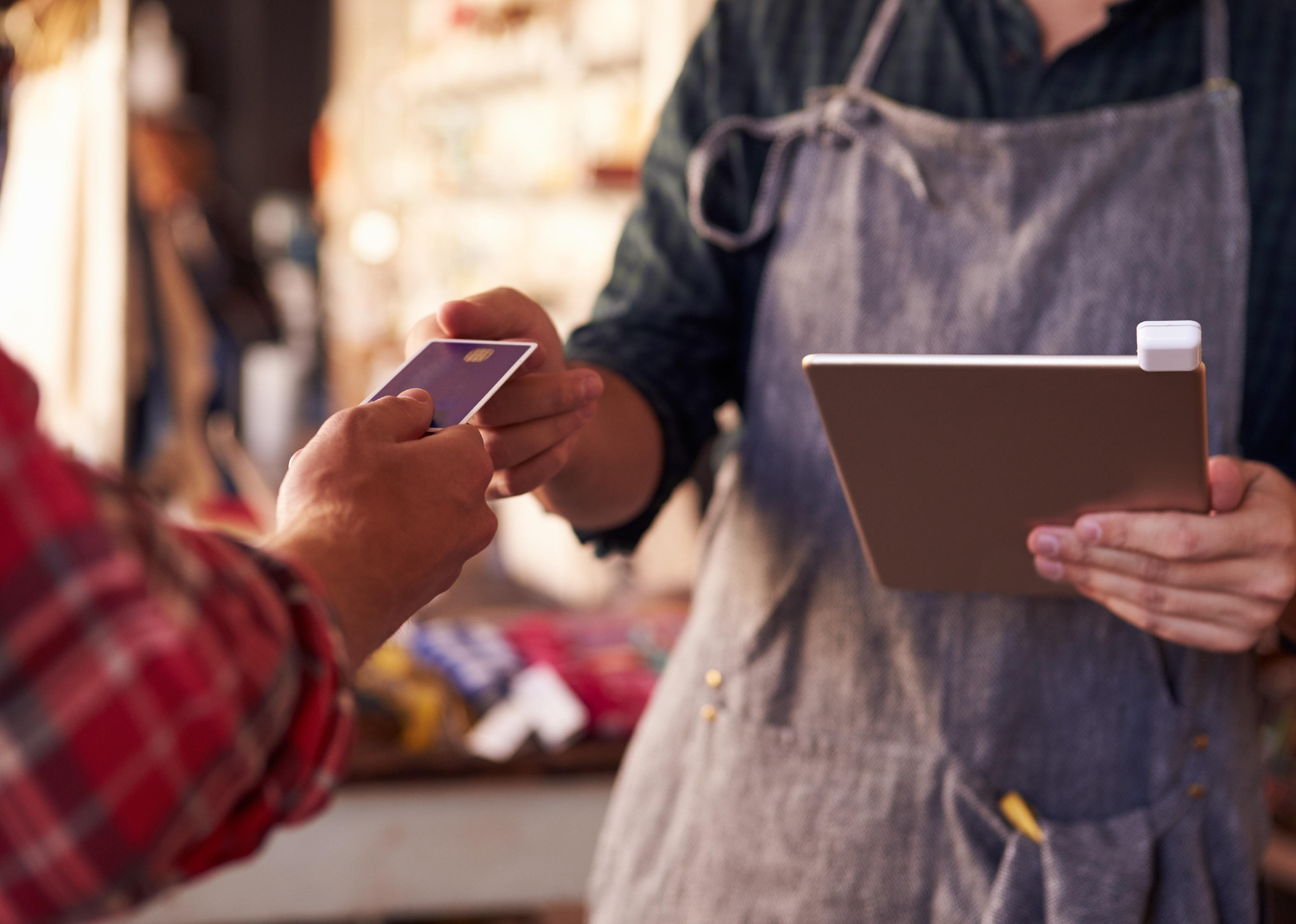 An employee holding a card reading device attached to digital tablet takes a credit card from a customer.
