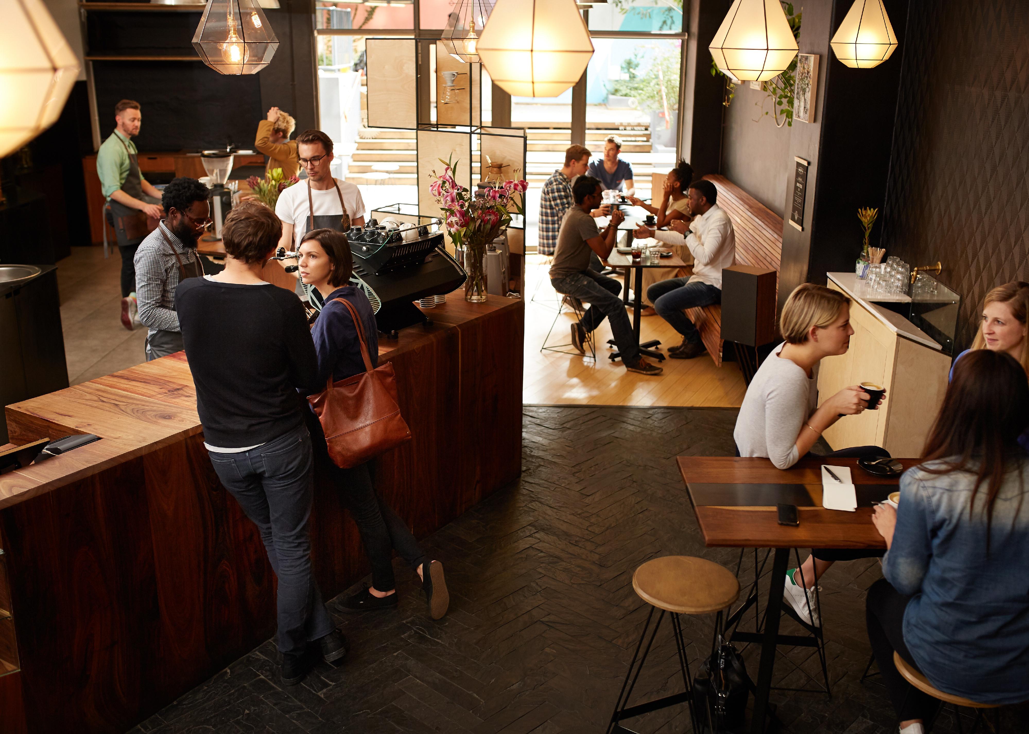 Customers waiting at counter in a busy modern coffee shop.