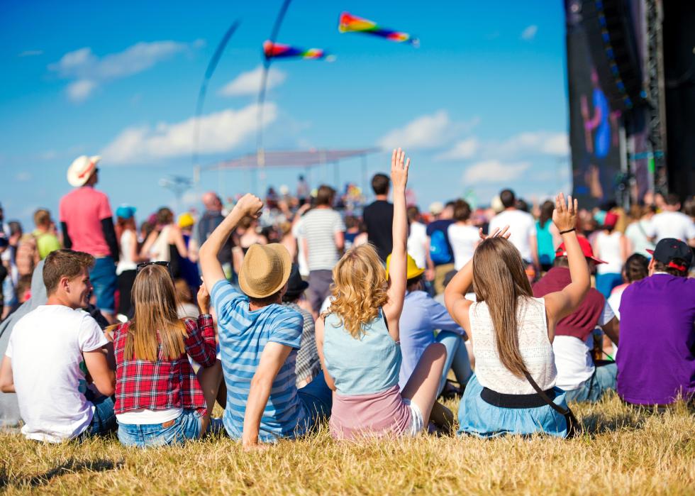 People sitting on the ground in front of an outdoor stage.