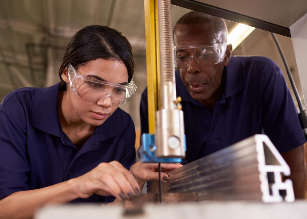 Carpenter training female apprentice to use a mechanized saw