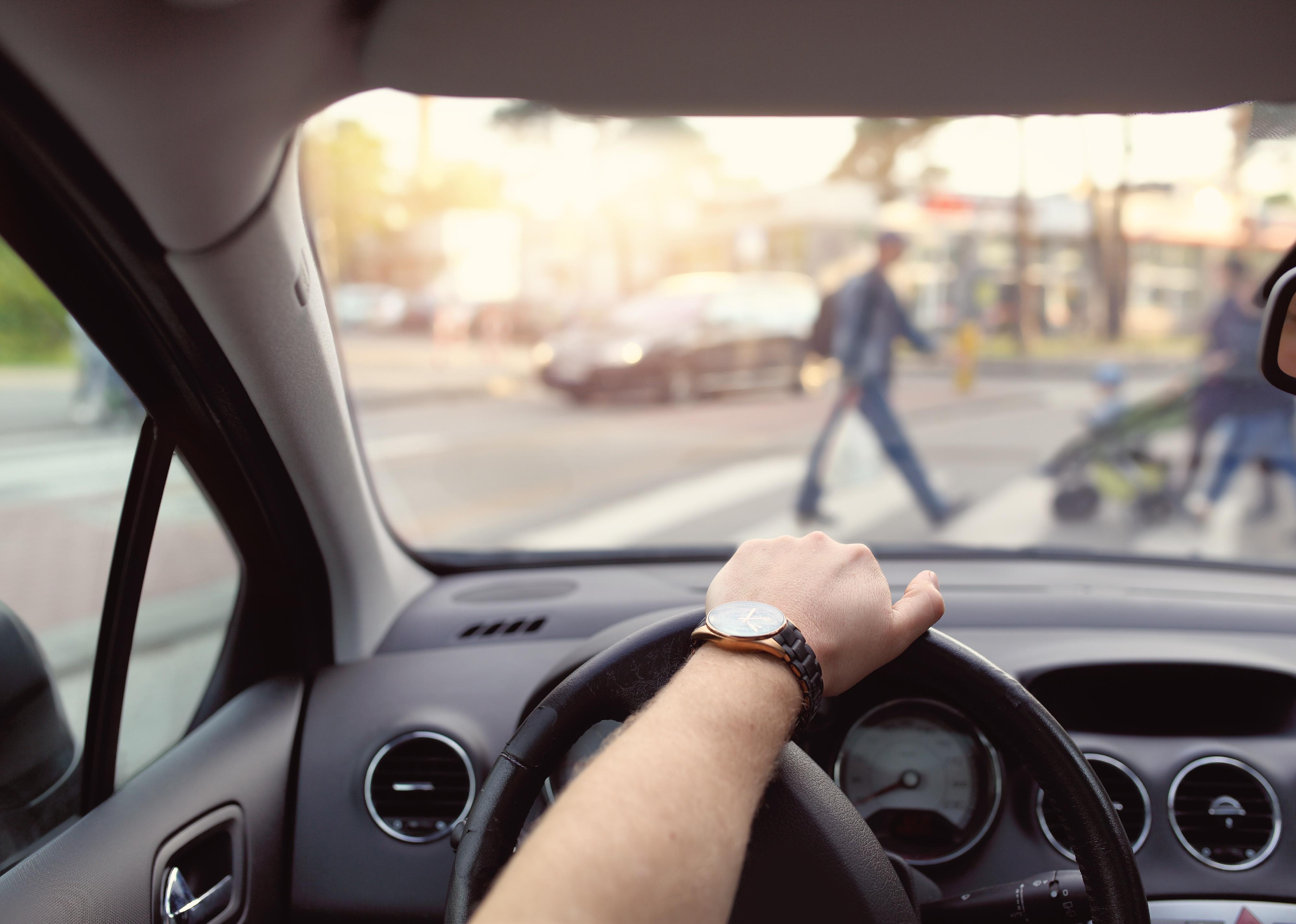 Driver with hand on wheel and pedestrians in front