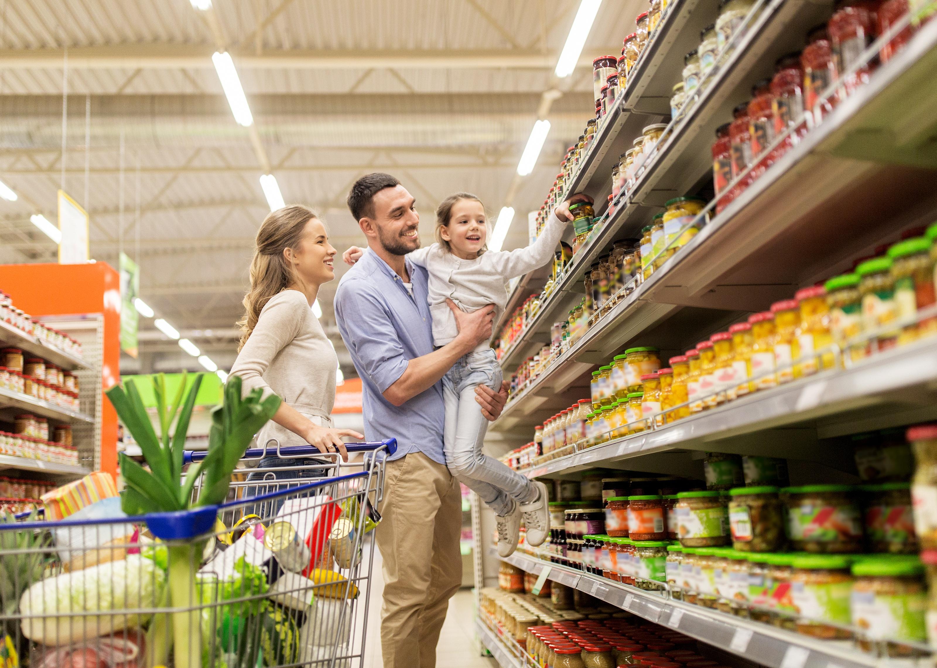 Happy family with child and shopping cart buying food at grocery store.