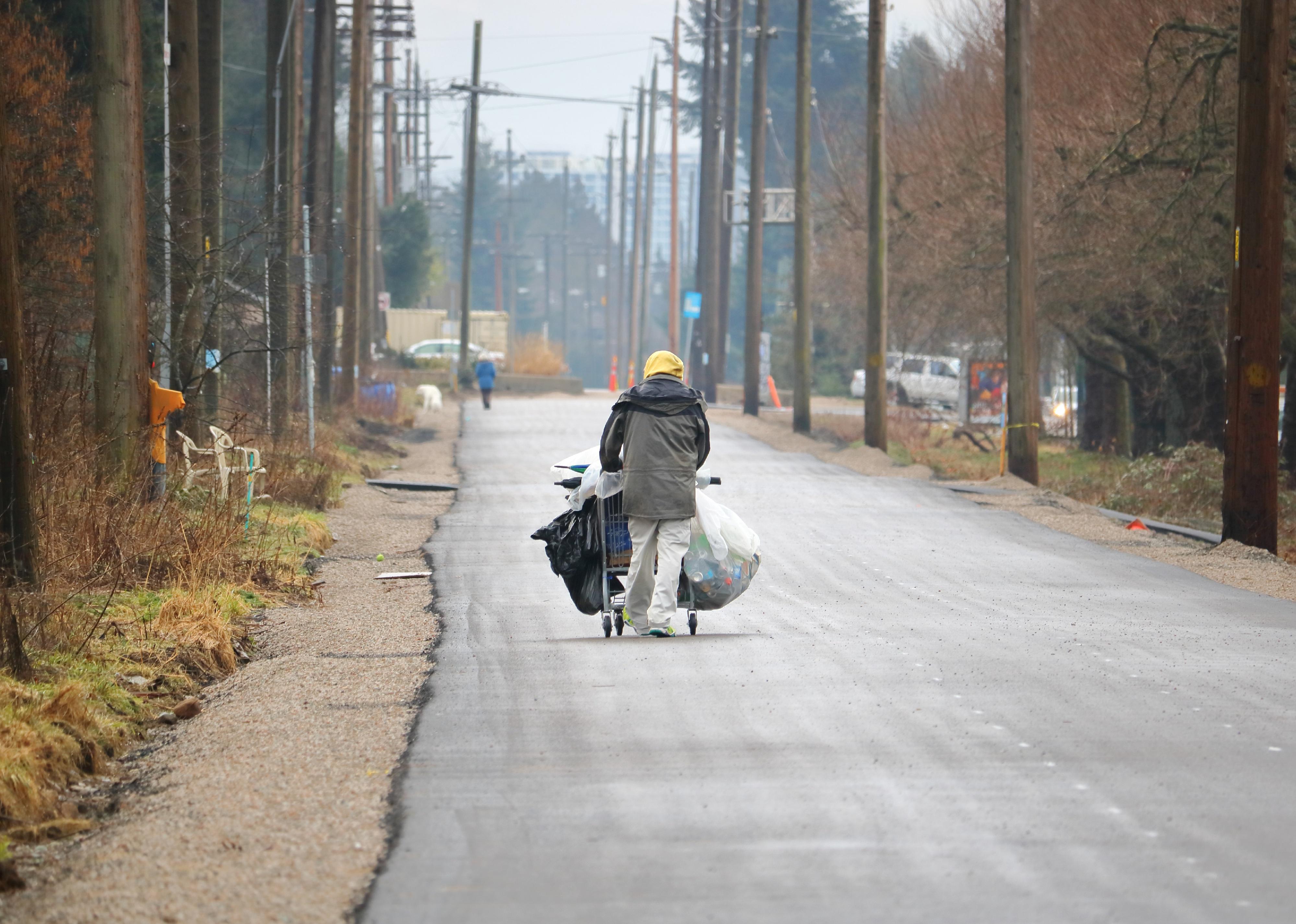 A homeless street person pushes a cart full of discarded bottles and cans.