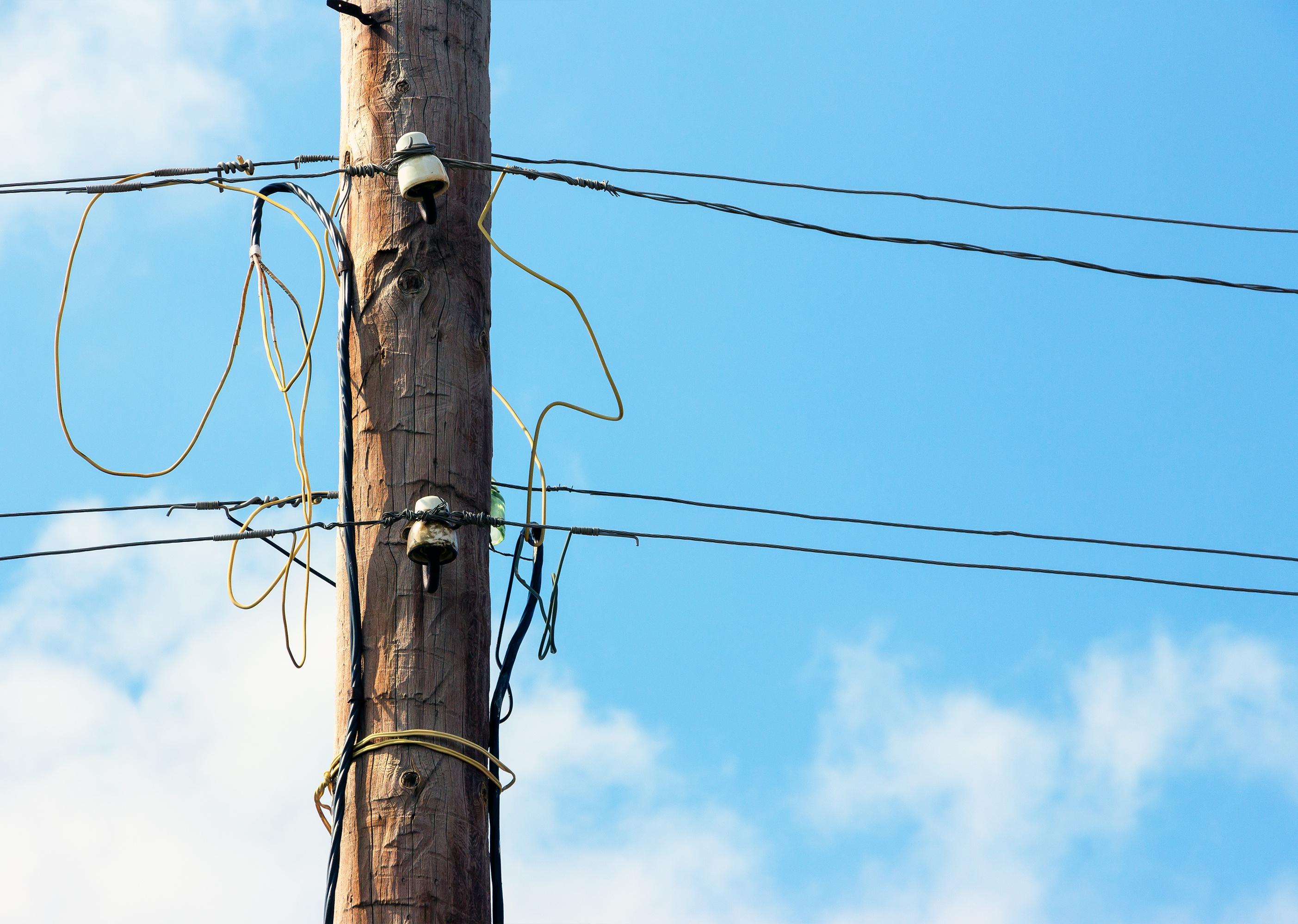 Old wooden pillar with power line against the blue sky.