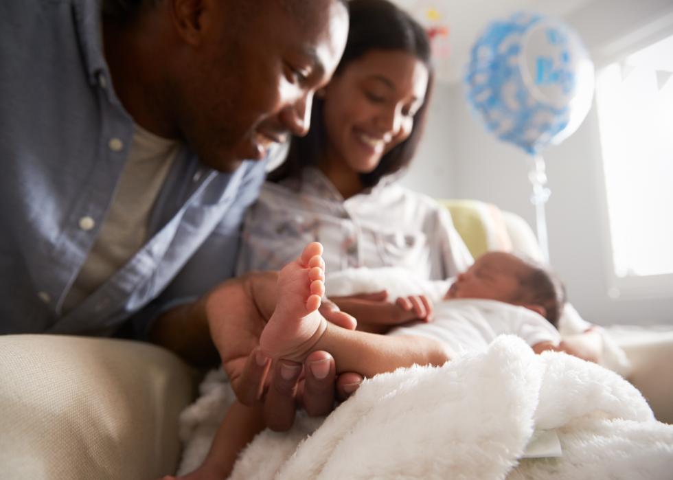 New parents smiling, holding their baby in the hospital.