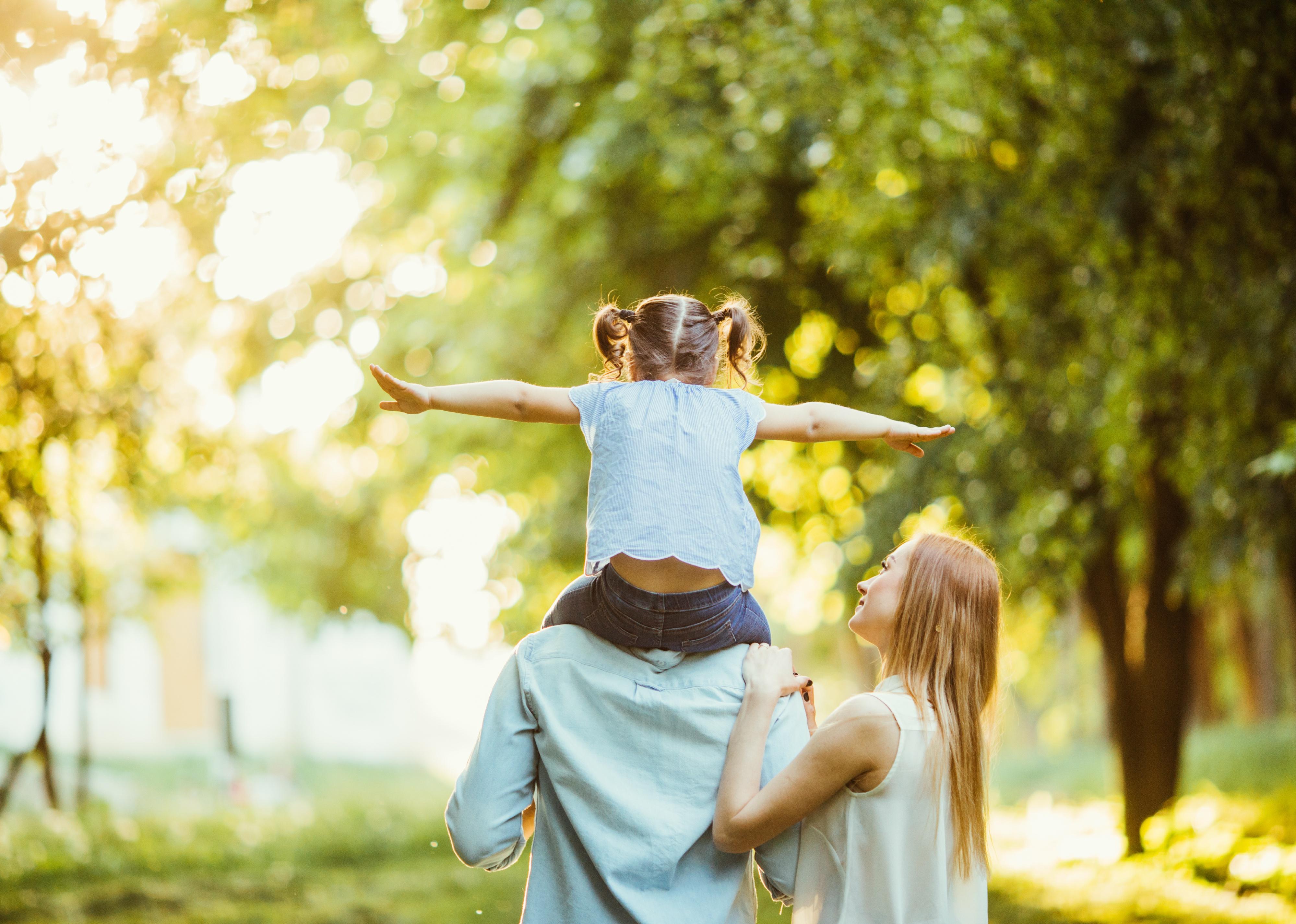 Back view of a little girl on fathers shoulders and mom walking alongside.