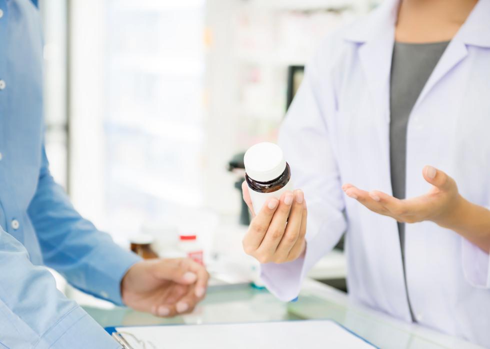 Pharmacist holding medicine bottle giving advice to customer.