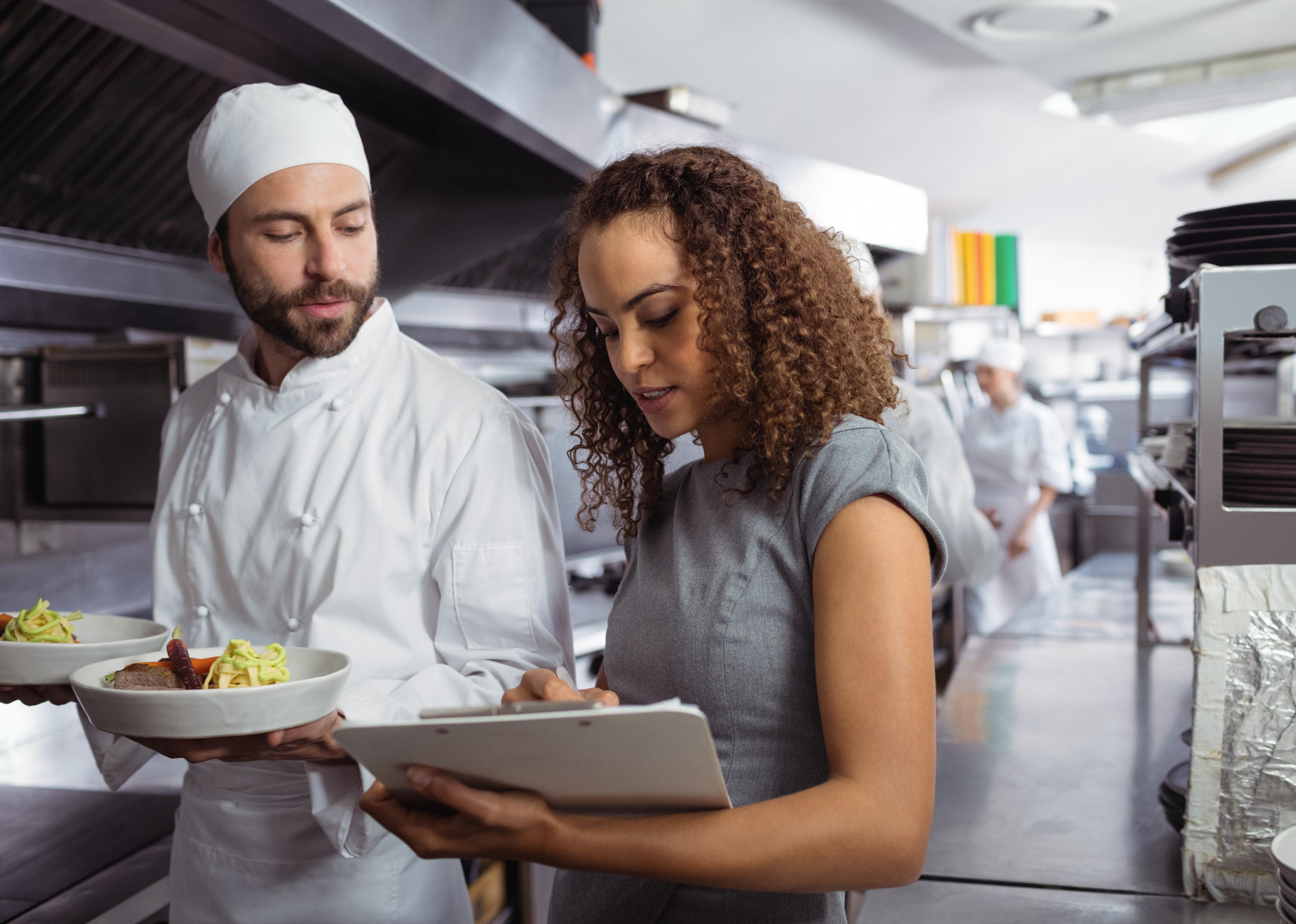 Restaurant manager and chef discuss notes on clipboard.