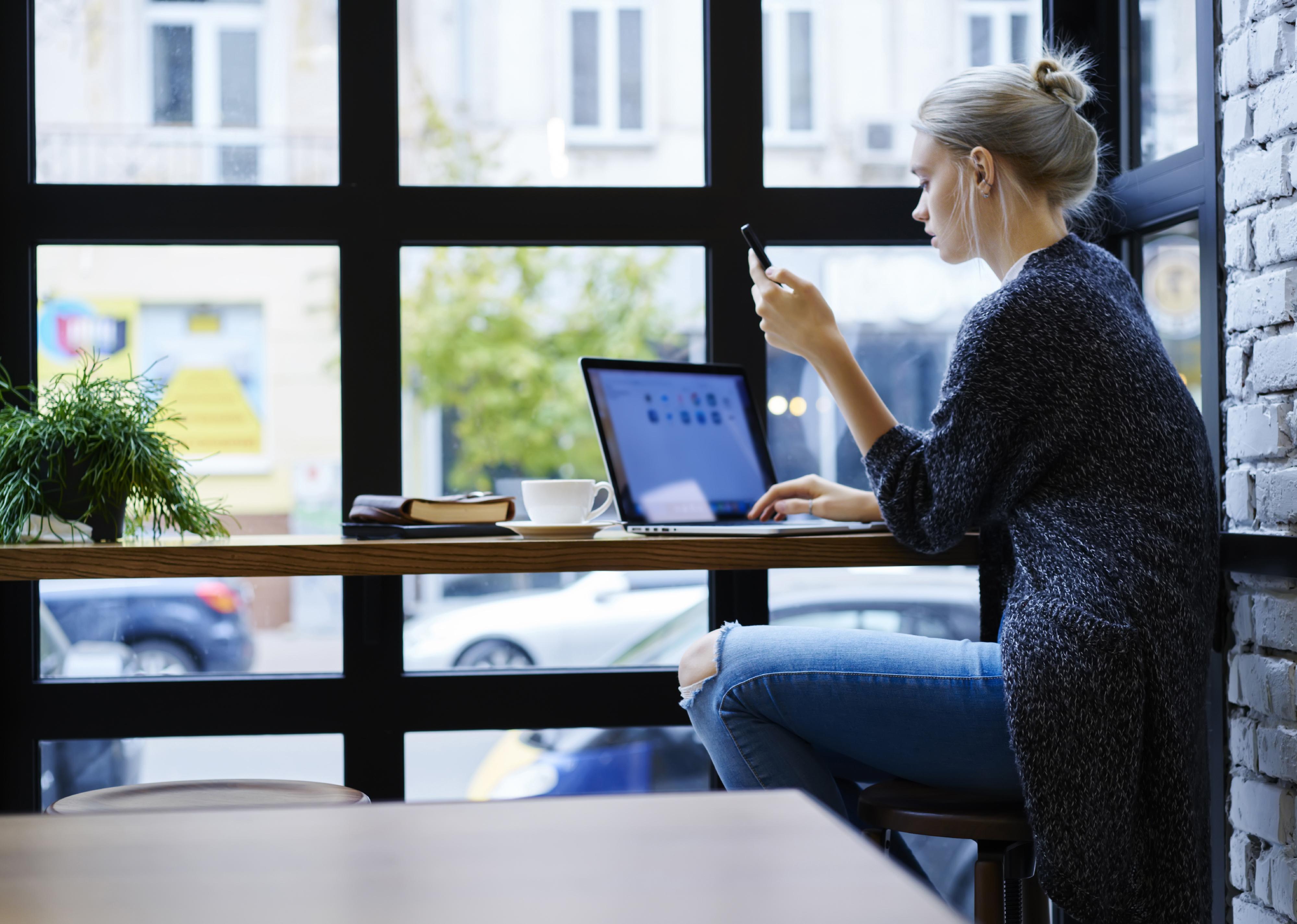 Woman with laptop looking at phone
