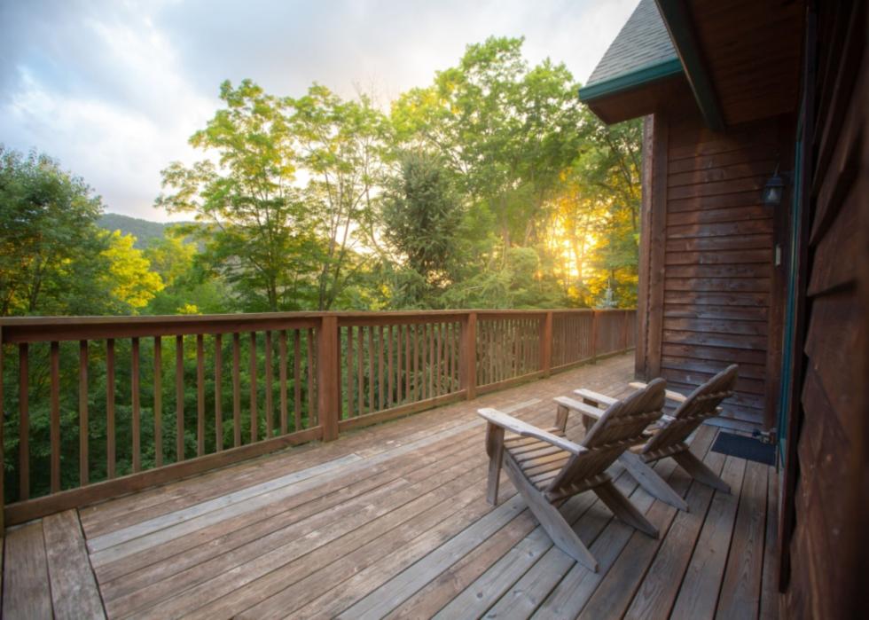 Two adirondack chairs on a wooden deck overlooking a forest.