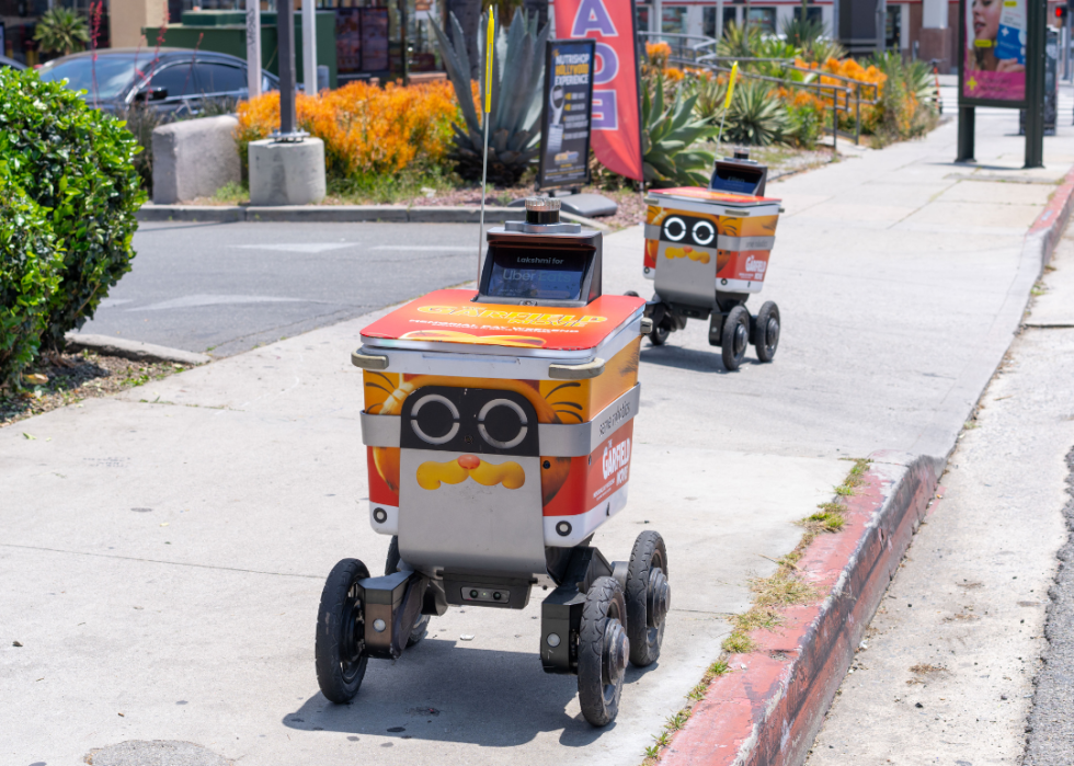 Two delivery robots in the city going down a sidewalk.