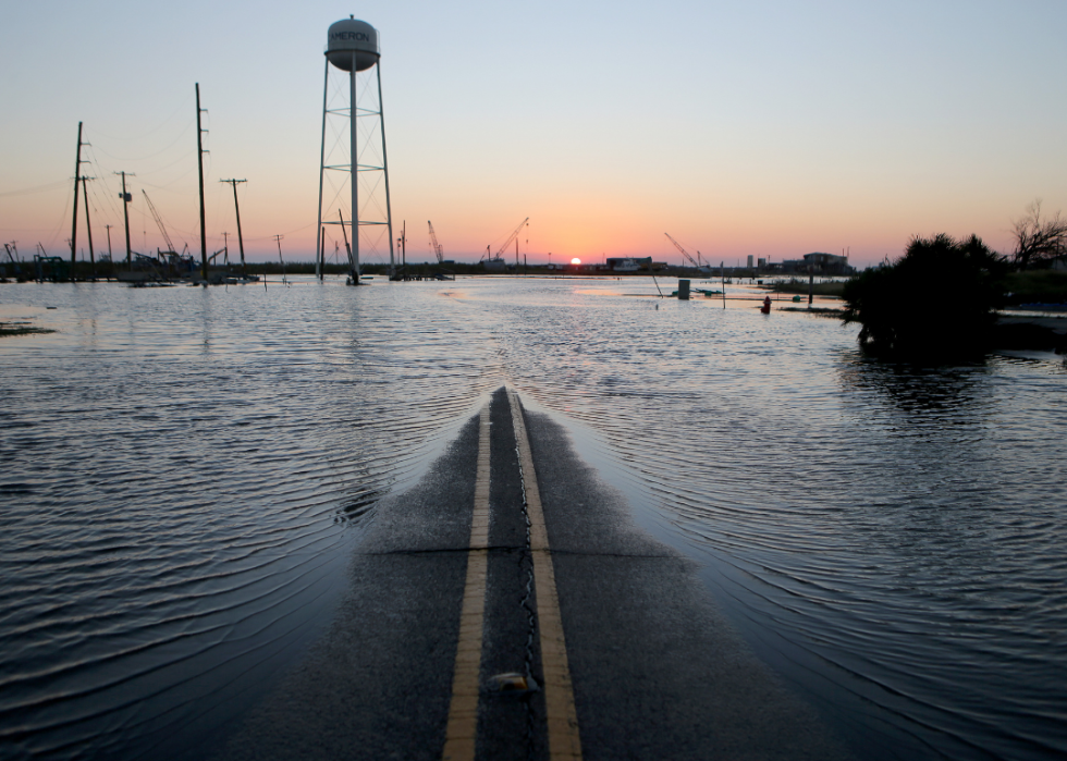 With the sun setting in the distance, only a small sliver of road is seen with the rest of the surrounding area covered in flood water.