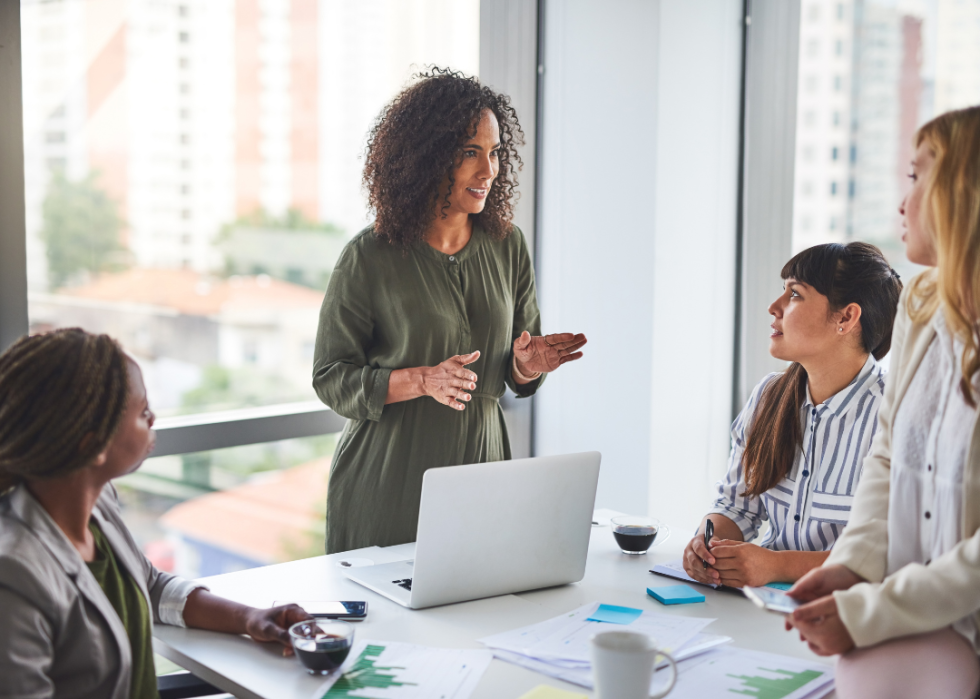A manager positively talks to three other women in a meeting in a brightly lit office.